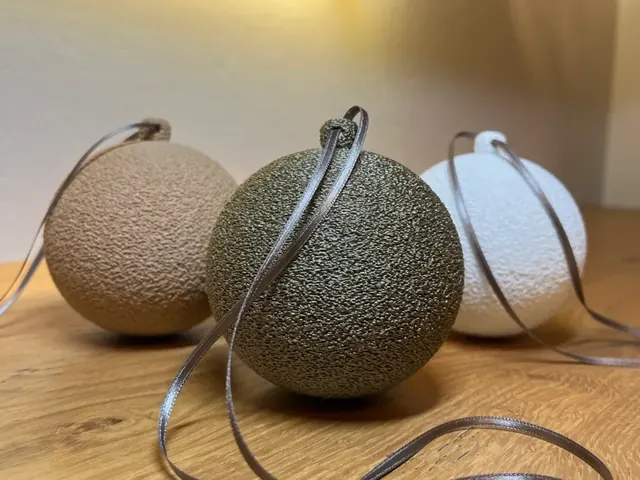 Bolas de Natal com superfície texturizada em tons claros e escuros, com detalhe para pendurar